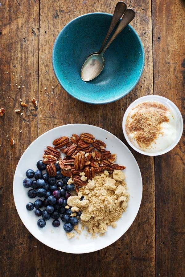 Plate with blueberries, pecans, and yogurt next to a blue bowl with spoons.