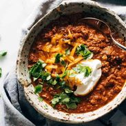 Bowls of chili with shredded cheddar, cilantro, and sour cream.
