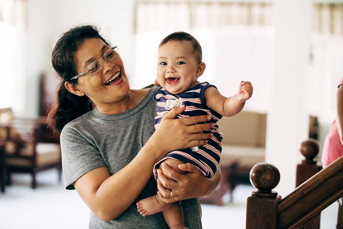 Woman with glasses holding a baby smiling at camera.