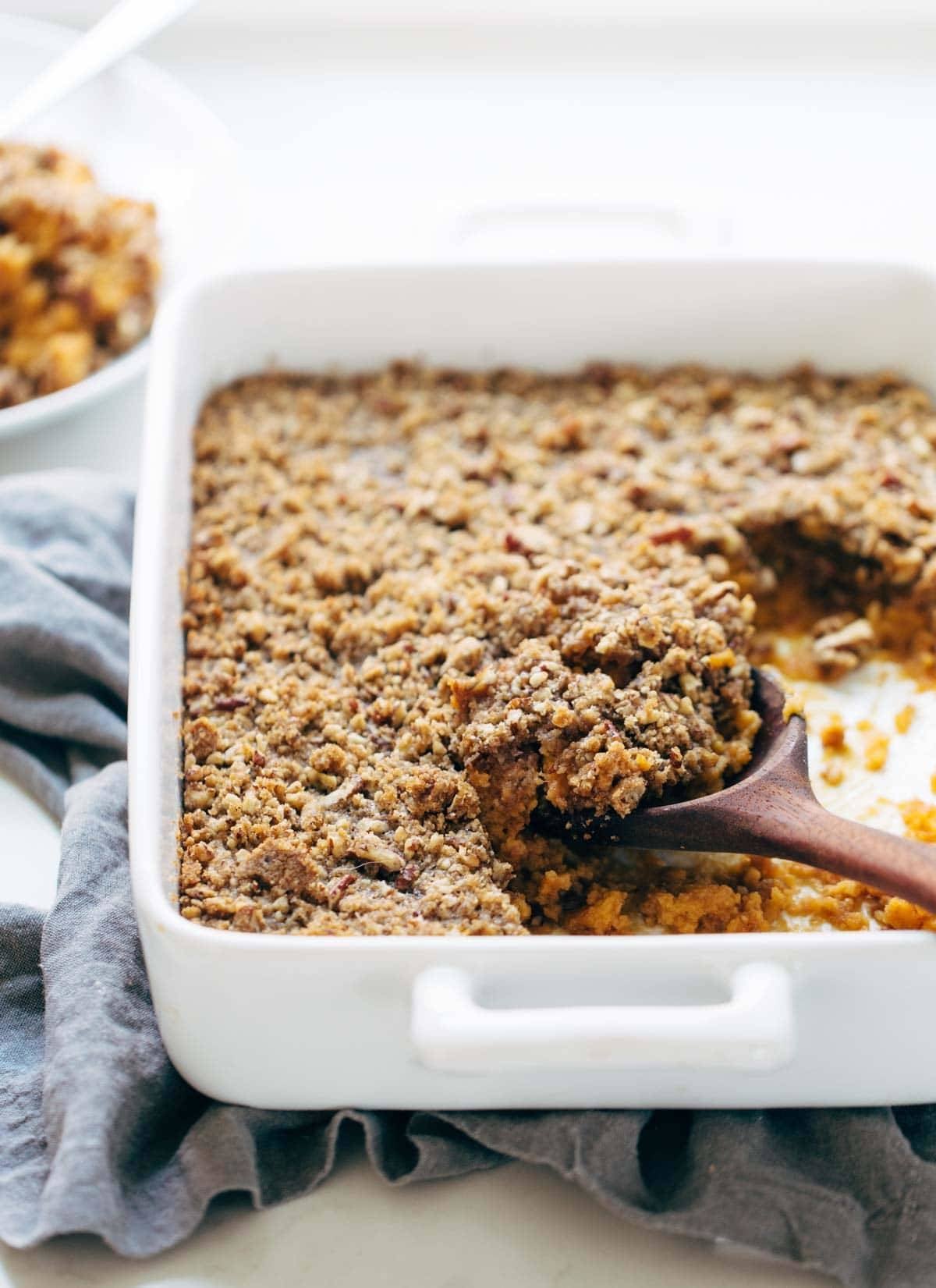 Sweet Potato Casserole with a crunchy brown sugar topping in a dish with a wooden spoon